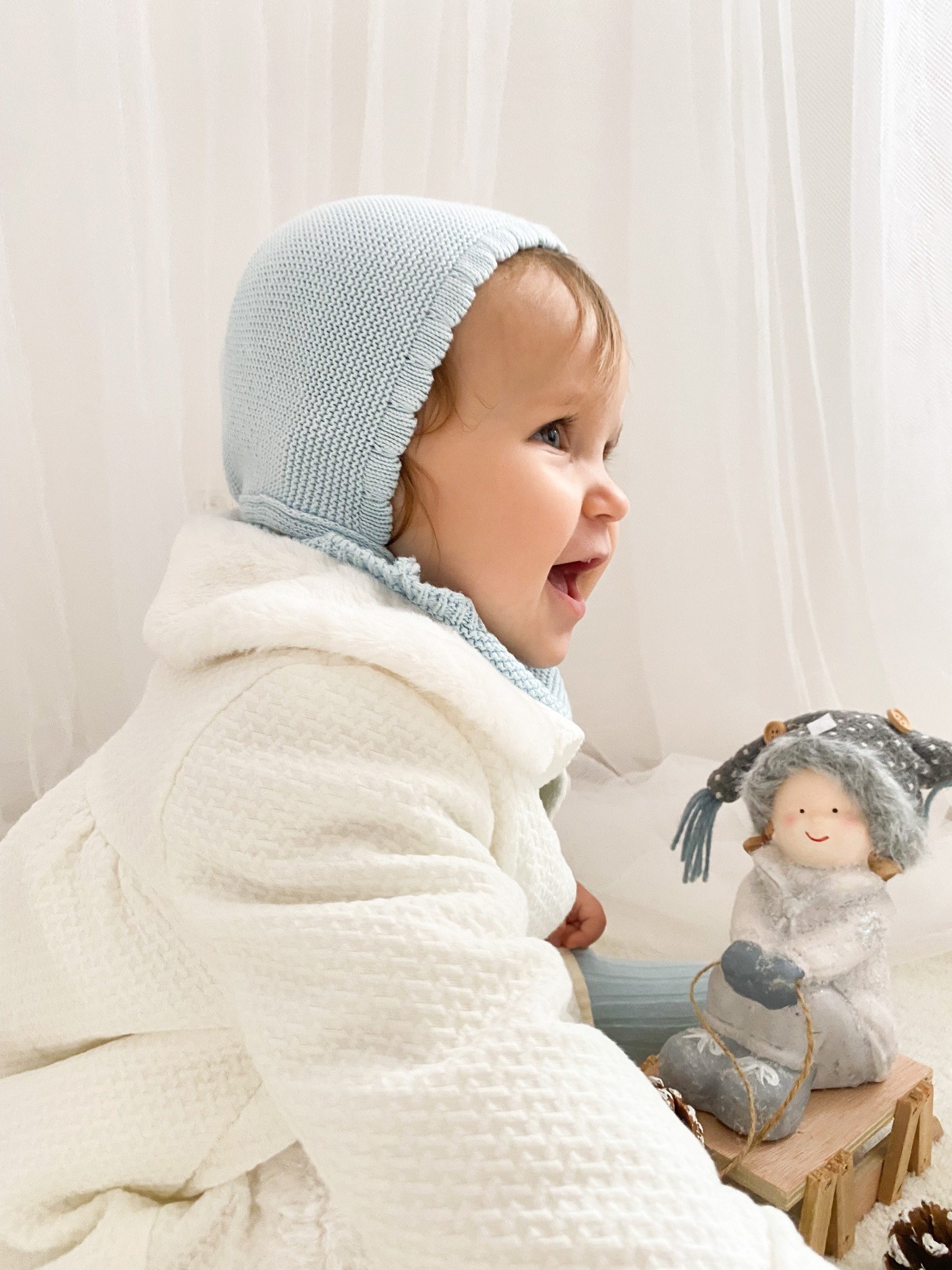 Niña sonriendo con capota azul y abrigo blanco